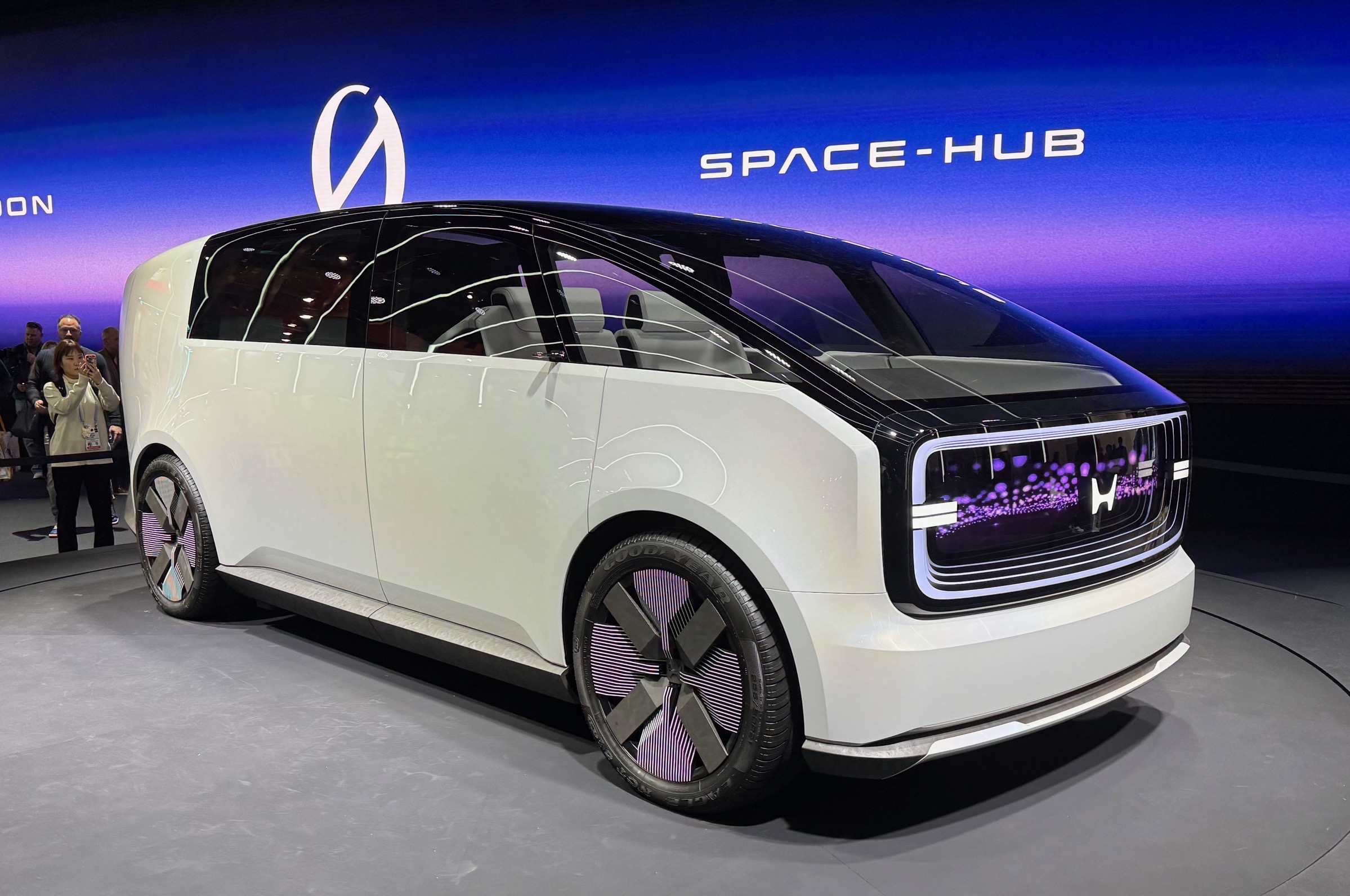 Honda Space-Hub. A boxy van with an all glass roof, high doors. it's on a spinning thing and it says Space-Hub behind it with the new silly logo.