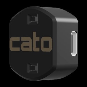Cato device is a small (1.5"x1.5") black rounded rectangle and about 1" thick. It has two small black rectangular protrusions top and bottom on the face and the word "cato" printed in gold lower-case print. A small rounded rectangular opening is located on one side of the device.