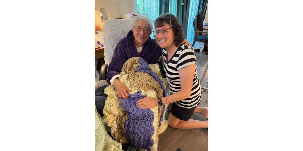 An elderly woman with grey hair smiling and hugging me with the blanket on her lap. we both look very happy.