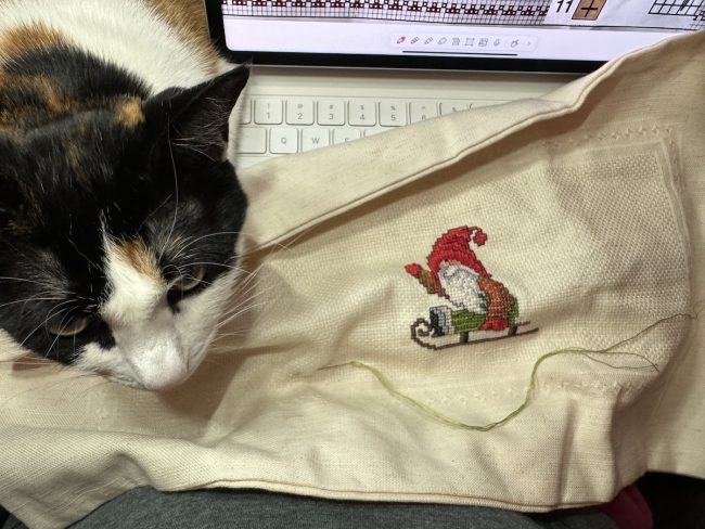 calico on my lap while cross stitching Christmas gnome with iPad in the background showing the pattern