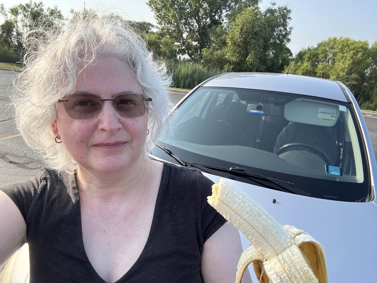 Marina and her prize banana. She has white hair, and a smirk on her face. she's taken a bite of the banana already.