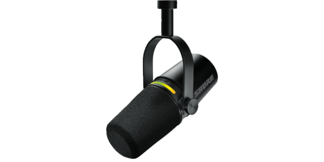 Shure mv7+ hanging down in a stirrup, probably attached to a boom arm. The mic is maybe 8 inches long with the foam mic input end pointed slightly downwards. there is a colored ring over the top.