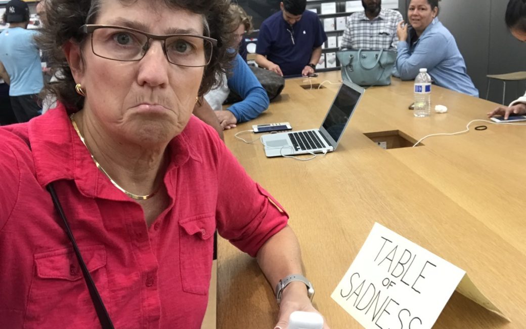 Allison sitting at the genius bar with a sign that says table of sadness made by steve
