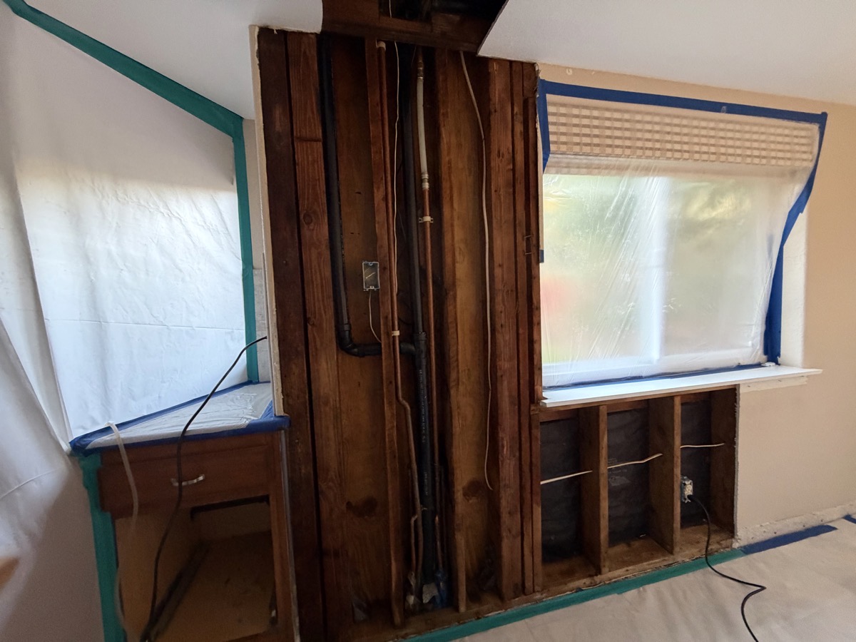 Kitchen wall removed inside tent showing pipes and raw wood.jpeg Kitchen wall removed inside tent showing pipes and raw wood.