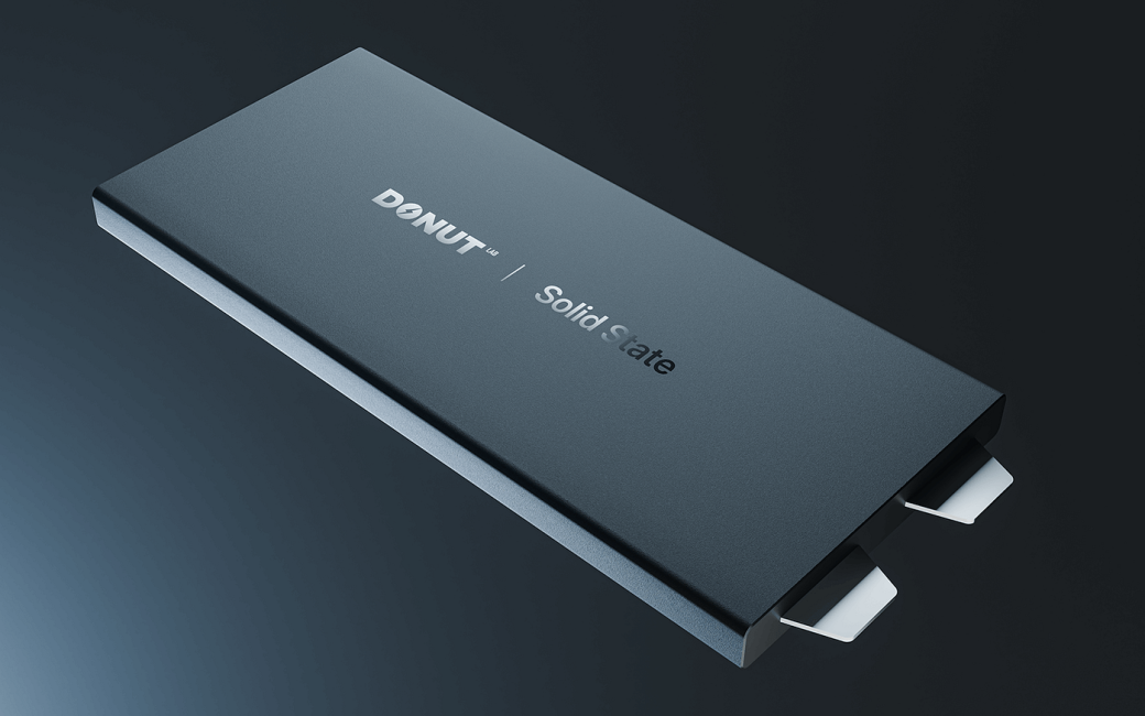 Slim, dark gray rectangular solid-state battery labeled “DONUT LABS | Solid State,” shown at an angle with two metal connector tabs protruding from one end against a dark gradient background.