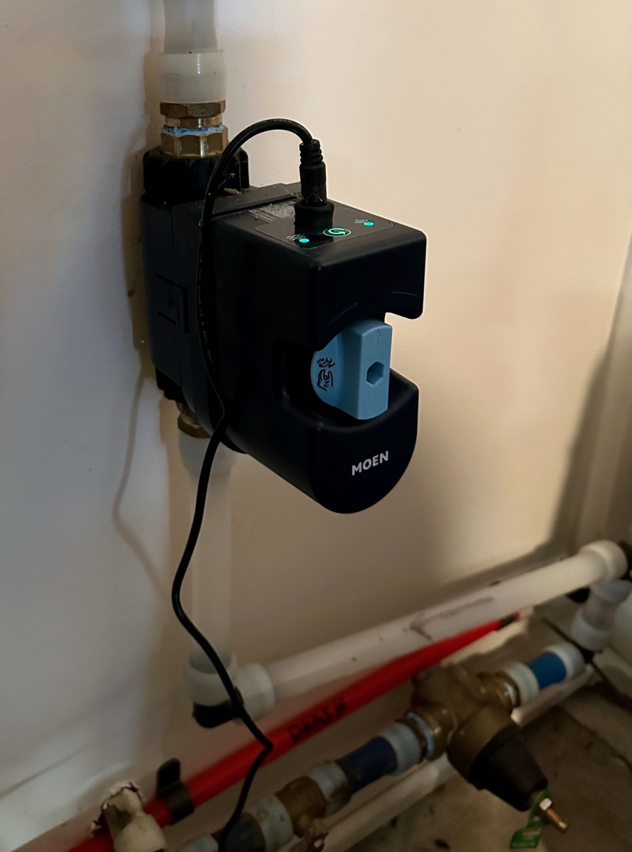 Wall-mounted Moen smart water shutoff valve installation showing in-line placement on main water supply, manual shutoff lever, status lights, and electrical connection..