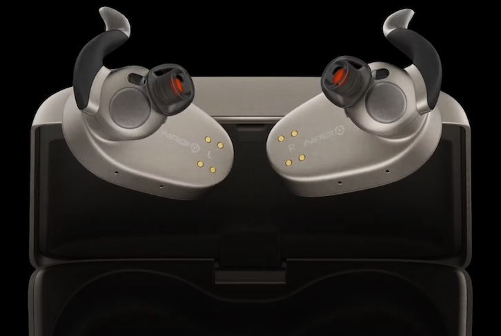 Close-up view of a pair of NaqiLogix neural earbuds. They are black and silver in color and futuristic in appearance as they rest in an open black charging case. Each earbud has a curved black ear hook, a cylindrical black bud with a red interior, and four small gold contact pins on the outer surface, set against a dark background.