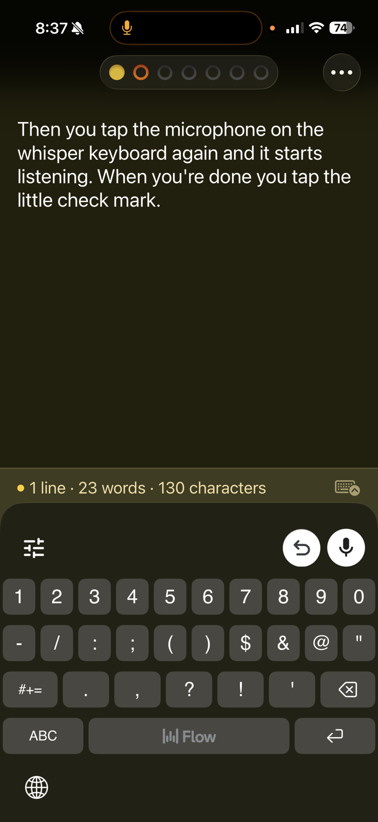 Wispr-iOS-Keyboard.PNG An iPhone screen displaying the active Wispr Flow custom keyboard in use within a text editing app. The keyboard has a dark theme and shows a number and symbol layout with a row of digits, punctuation marks, and special characters. At the top of the keyboard, a status bar reads "1 line, 23 words, 130 characters." An undo button and a microphone button with an active red recording indicator appear in the upper right of the keyboard. The text area above shows a dictated paragraph about using the Wispr keyboard's microphone and checkmark features.