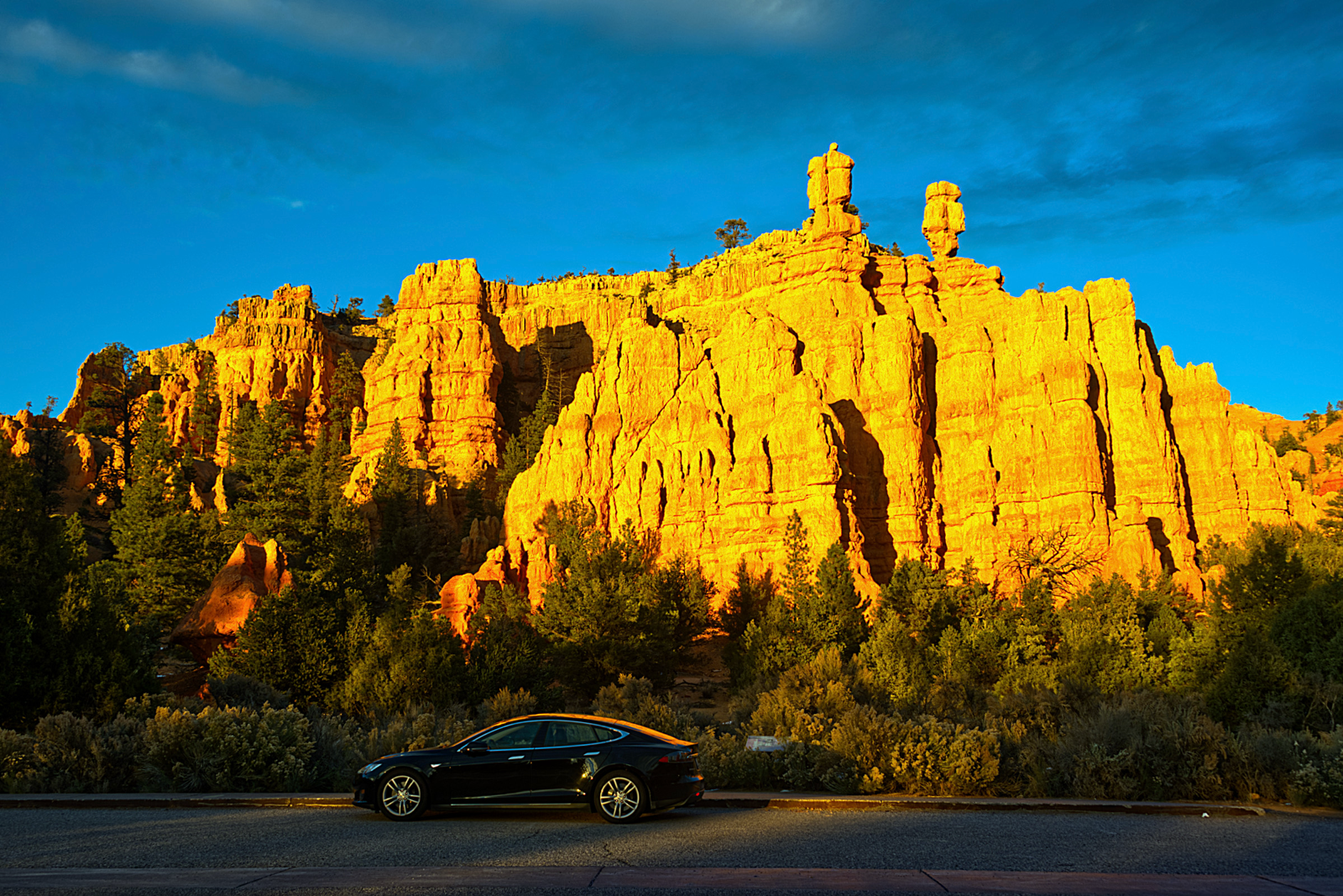 Ron Model S in Red Canyon Southern Utah. the car is super shiny and beautiful and the backdrop is dramatic cliff rocks bathed in an orange glow from the sunset with a rich blue sky behind.