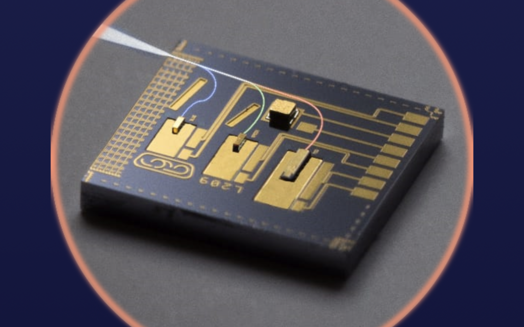 Close-up photo of a tiny photonic chip with gold circuit-like pathways and three labeled laser channels etched onto a dark surface. Colored lines illustrate red, green, and blue light paths converging toward a white output beam exiting the chip. The chip is shown against a dark gray background inside a glowing circular border.