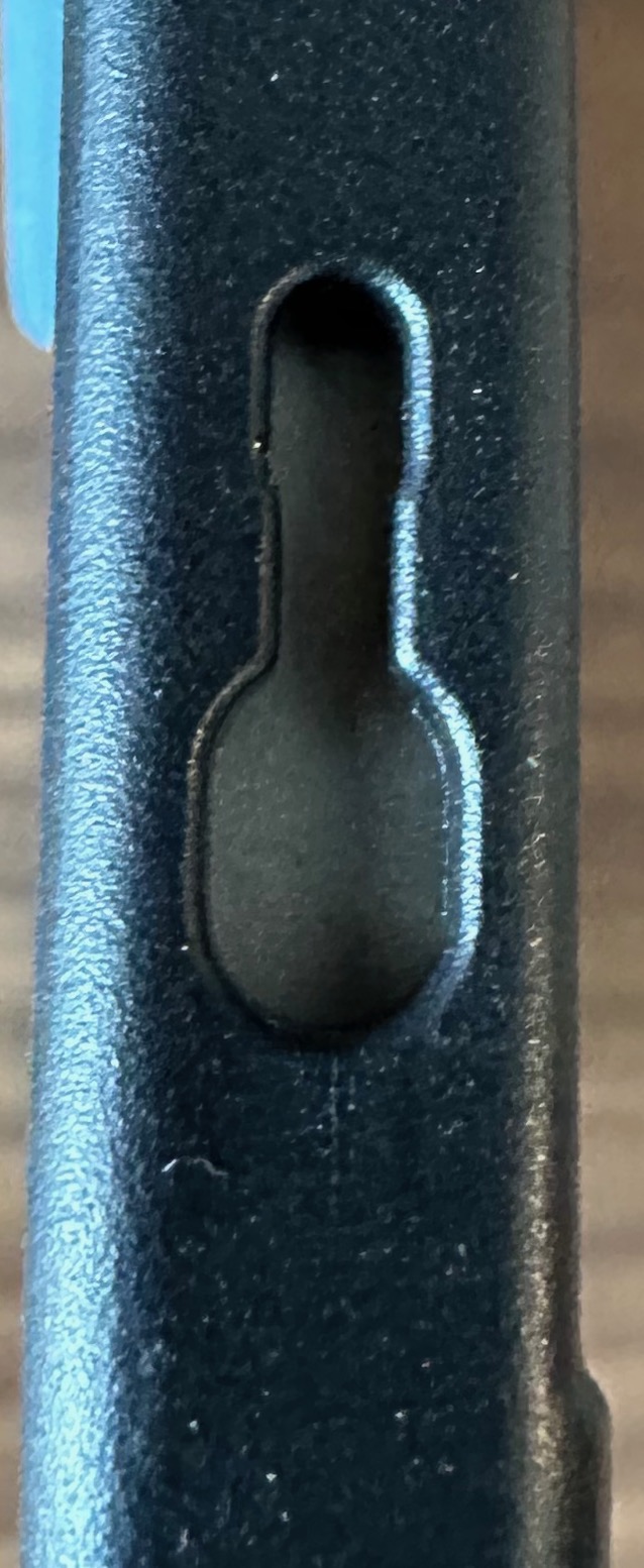 Keyhole-closeup-full.jpeg Closeup of a black keyhole-shaped slot in the edge of the Strapsicle case. The slot has a round opening sized to admit the head of the post, narrowing to a slit below that grips the post's stem.