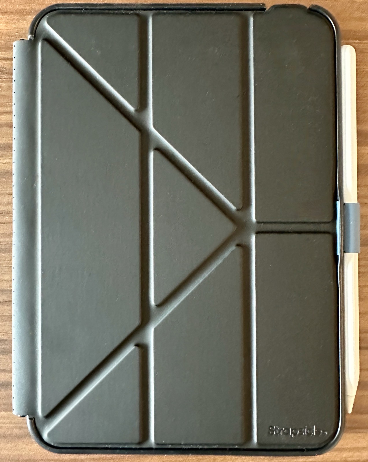 Strapsicle-front-cover-full.jpeg Front view of the Strapsicle case for iPad mini with the cover closed. The cover is dark gray and is scored with origami-style fold lines that form a fan of triangles, which is what lets it fold into multiple stand configurations. The Apple Pencil rides in an elastic loop on the right edge.