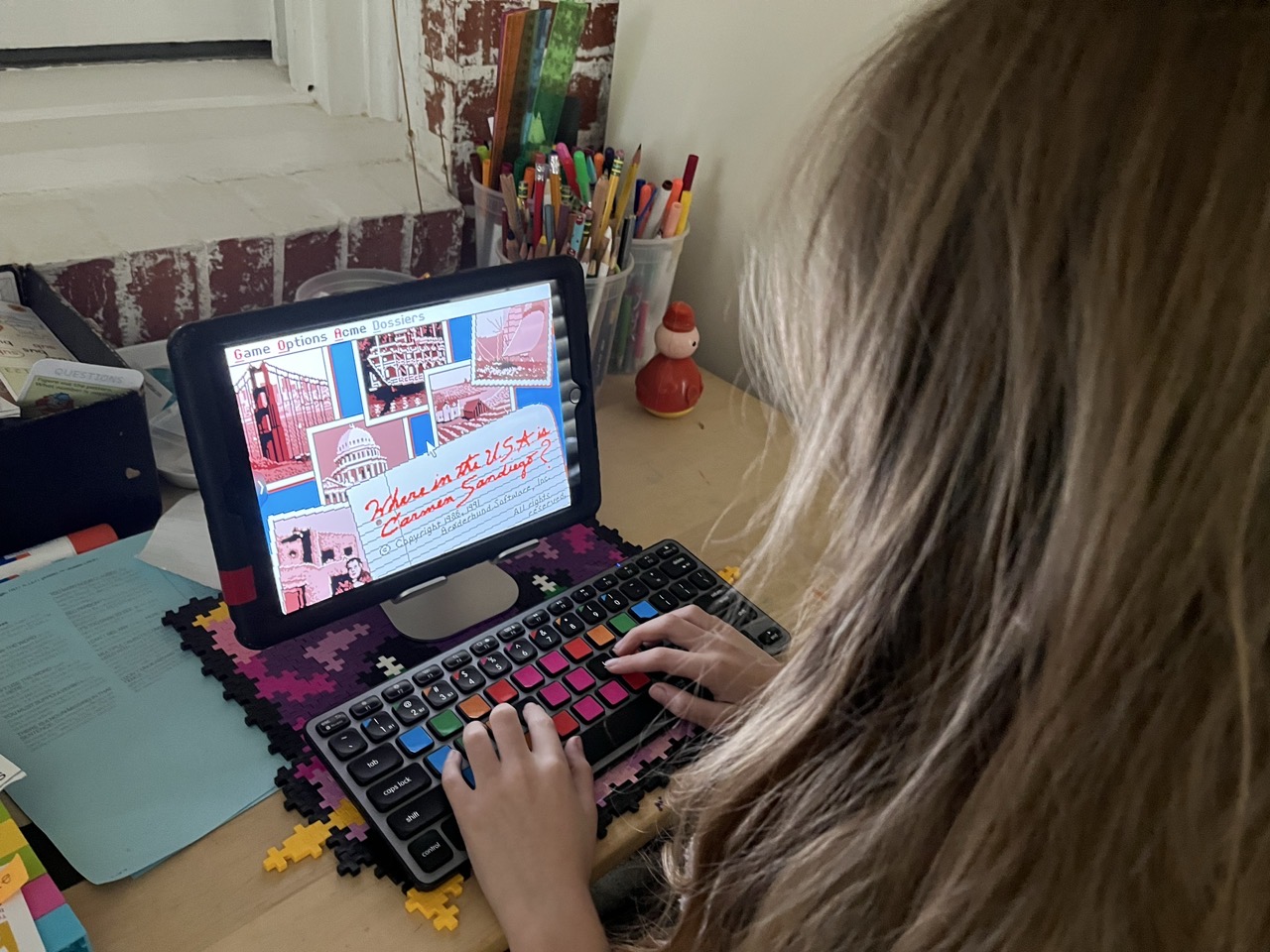 DOS Emulator Carmen Sandiego.jpeg Over the shoulder view of a young girl with an iPad showing DOS Emulator Carmen Sandiego.