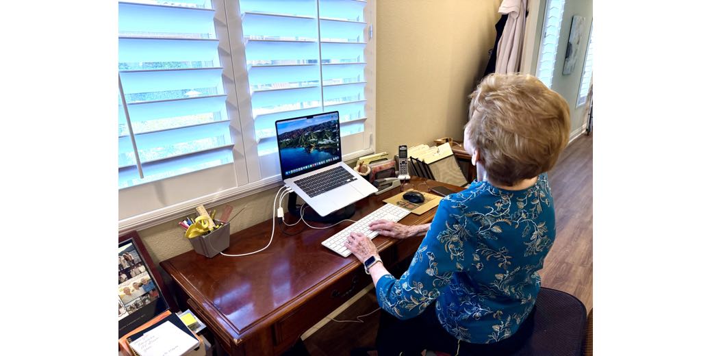 Merlee at her new desk showing off how empty it is as she works at her Mac. She's being silly looking up so high