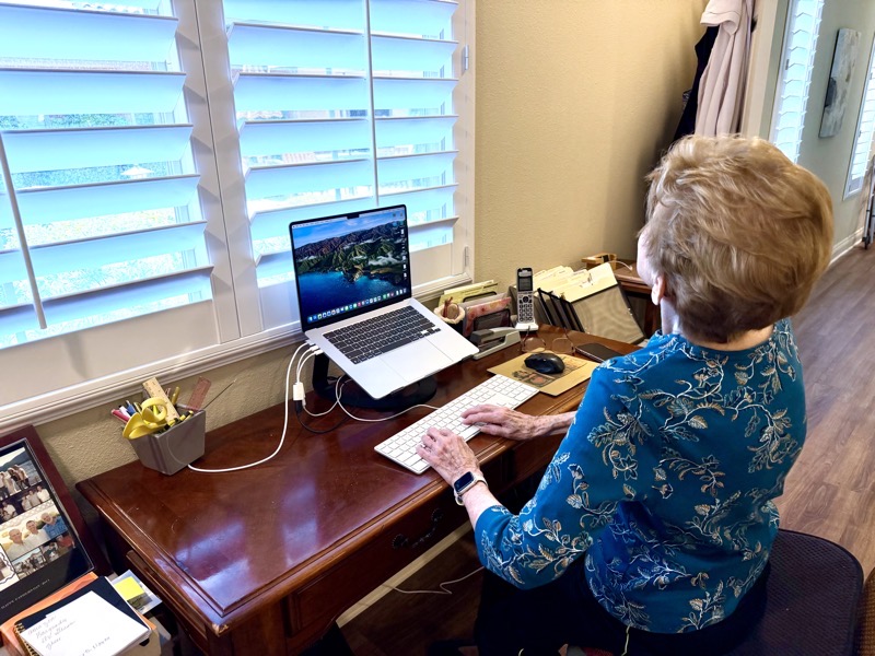 Merlee at her new desk showing off how empty it is as she works at her Mac. She's being silly looking up so high