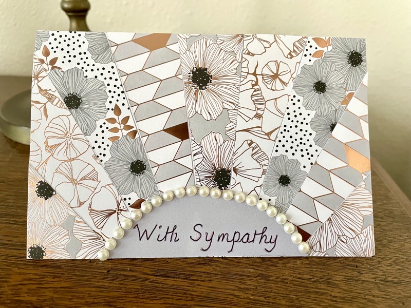 Sympathy card made by Merlee. it has ribons of different patterns radiating out from the bottom center, with an archway made of white beads around the words "with sympathy"